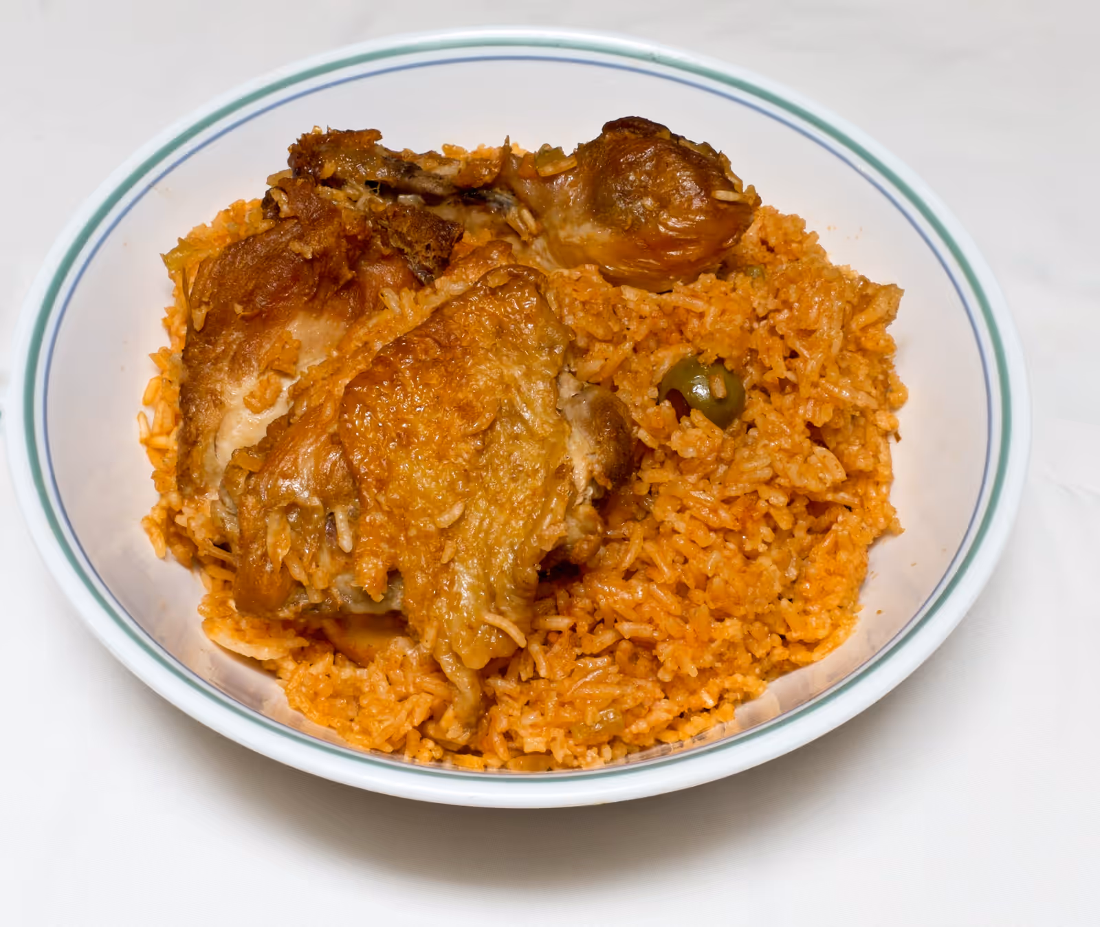 Locrio de pollo: orange rice, browned thighs and an olive, in a deep plate