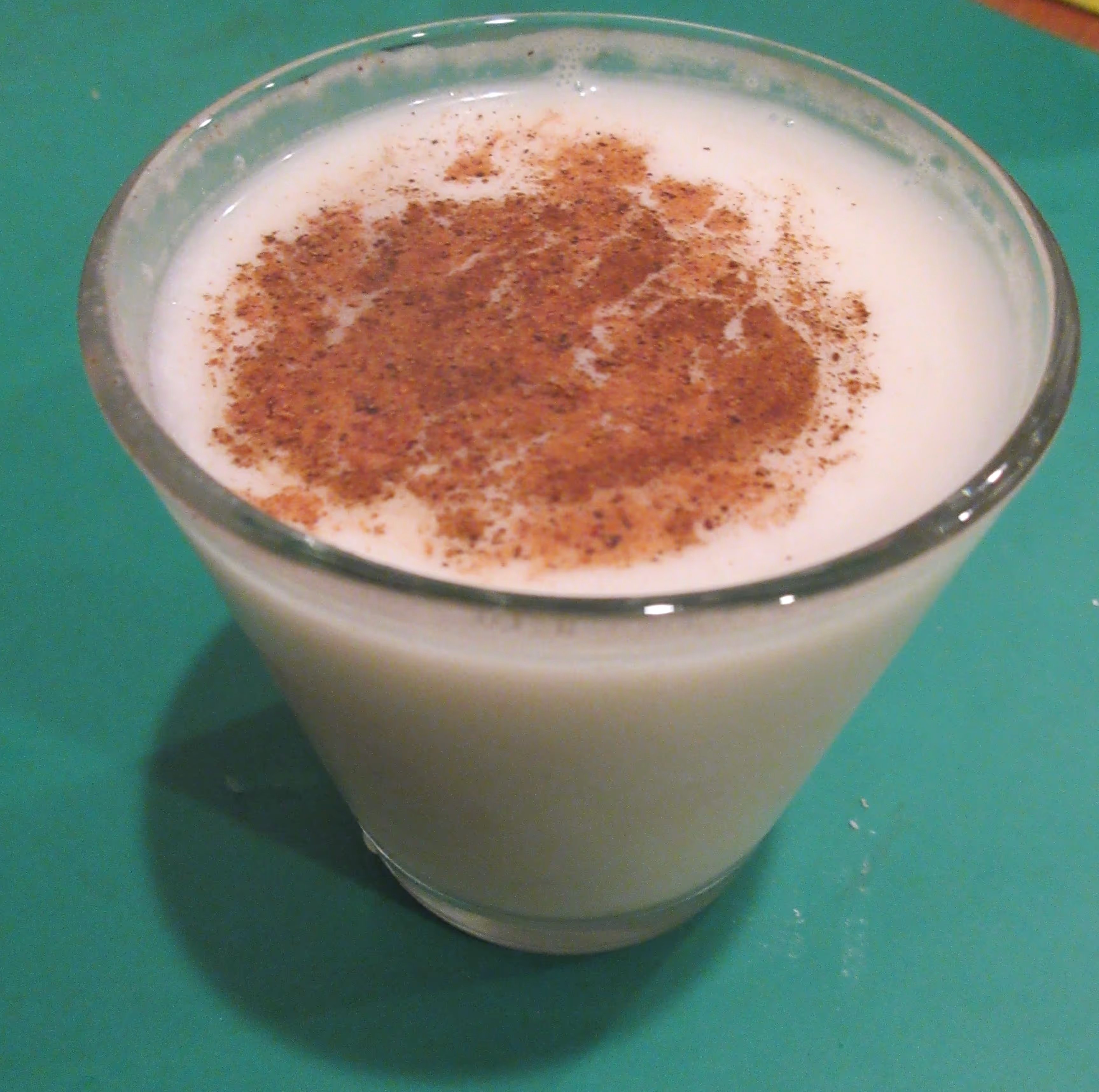 Close-up of a glass of coquito, ground cinnamon on the surface, on a green table