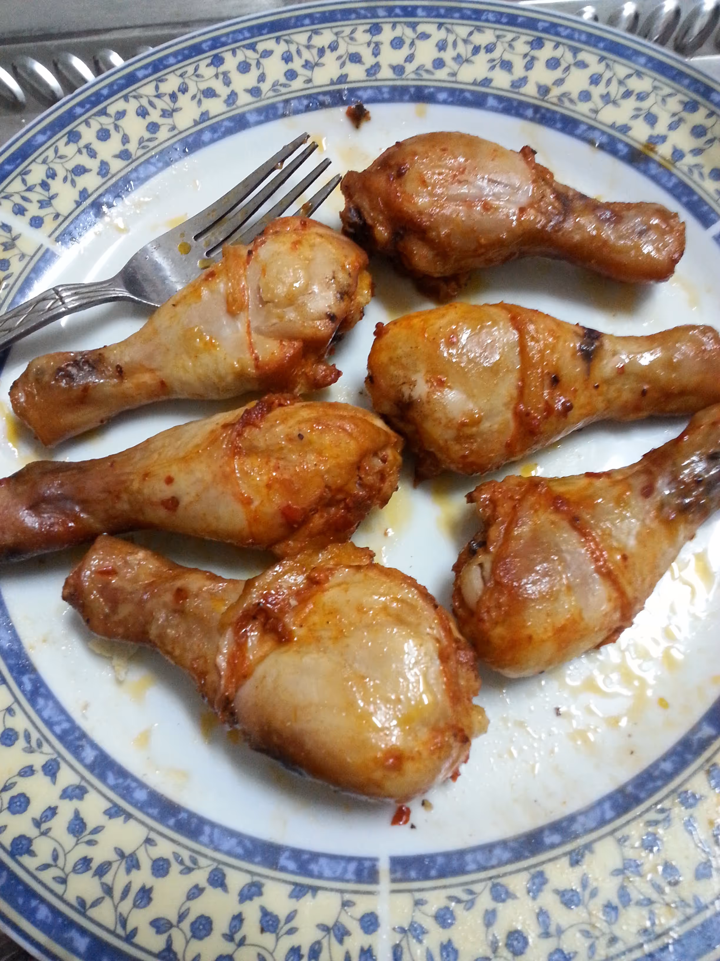 Six roasted chicken drumsticks on a white plate with a blue floral rim