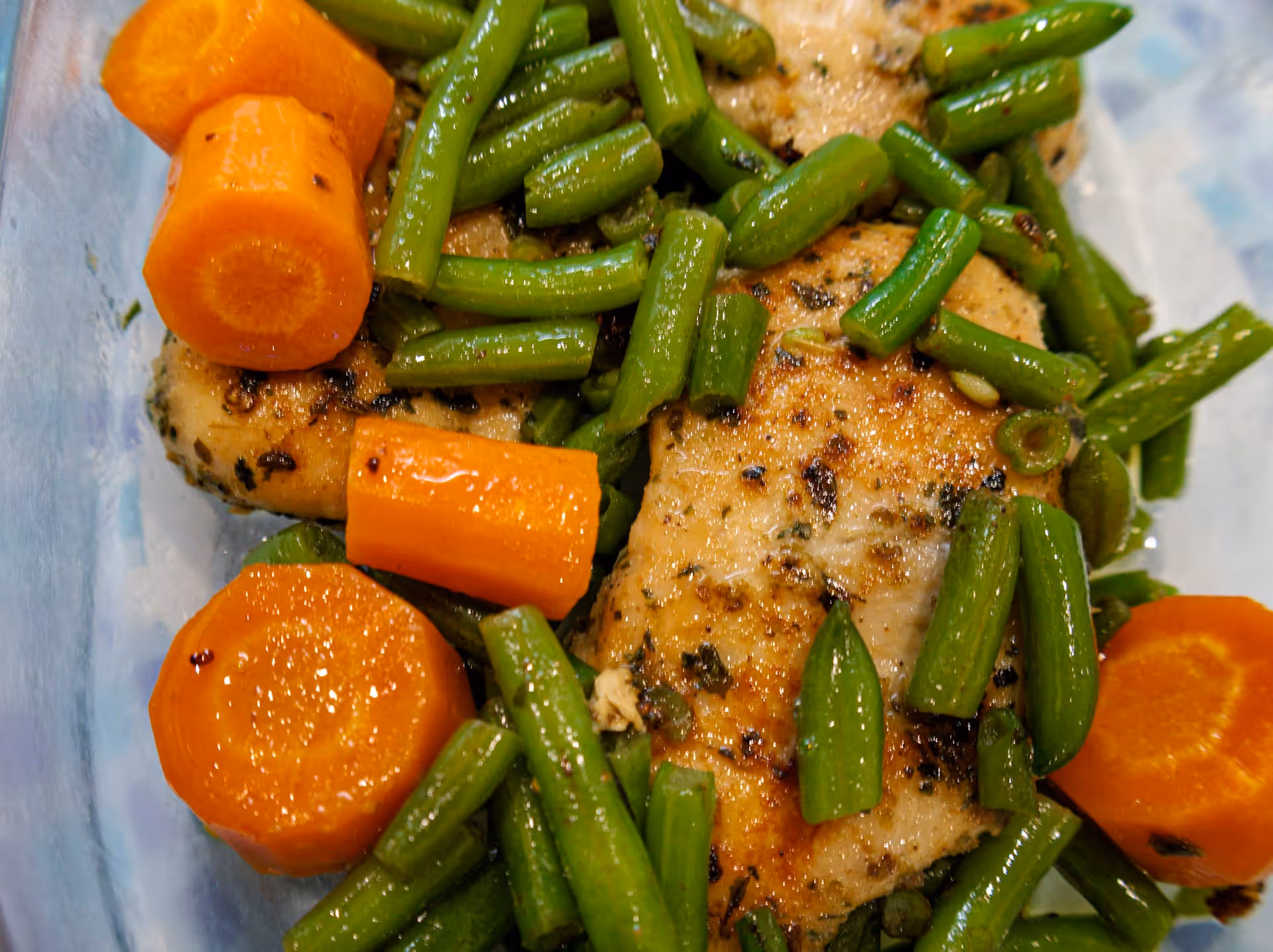 Two baked chicken breasts in a dish with green beans and thick carrot coins